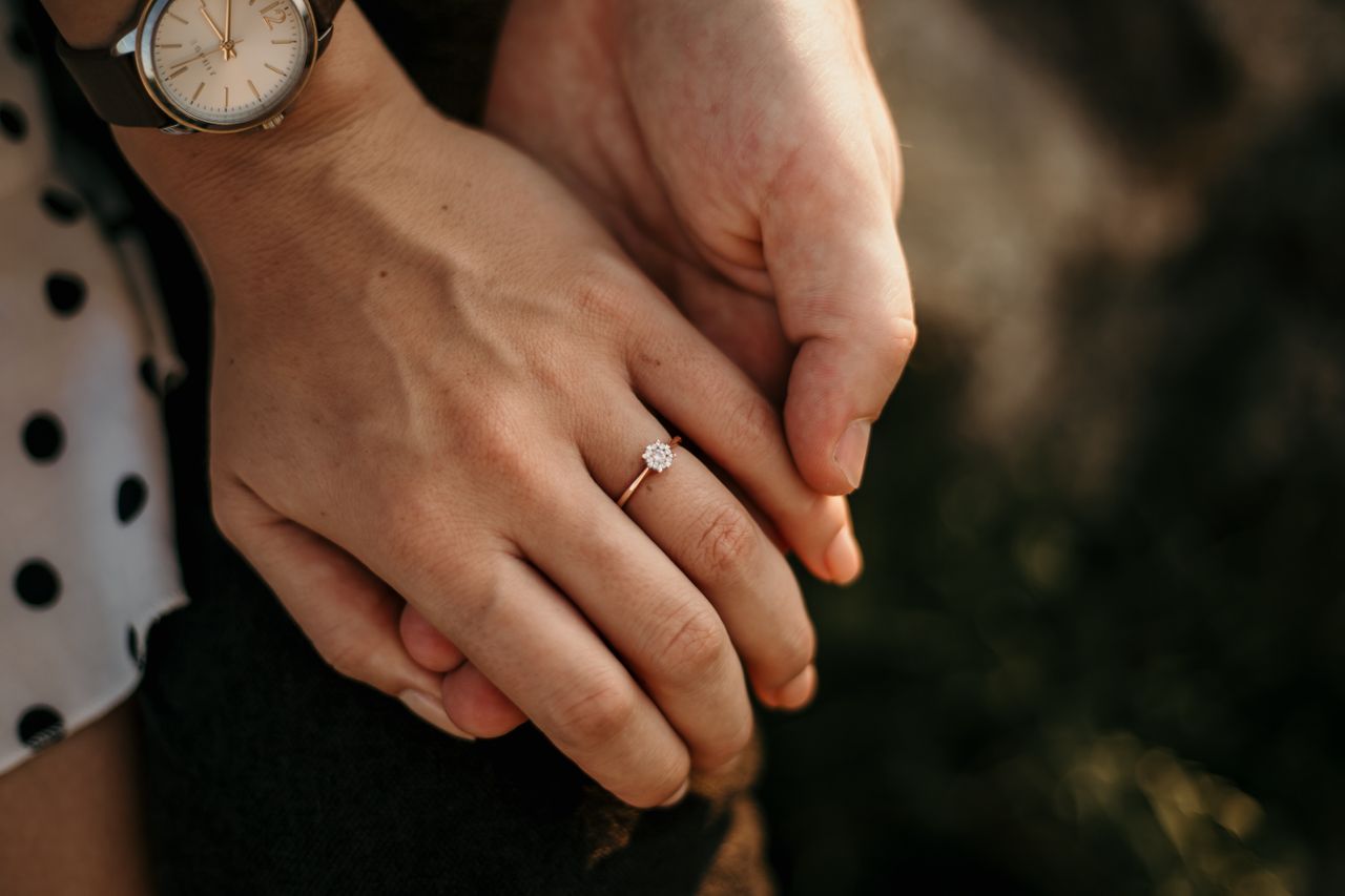 A close-up of a newly engaged couple holding hands, with focus on her simple yet elegant engagement ring.