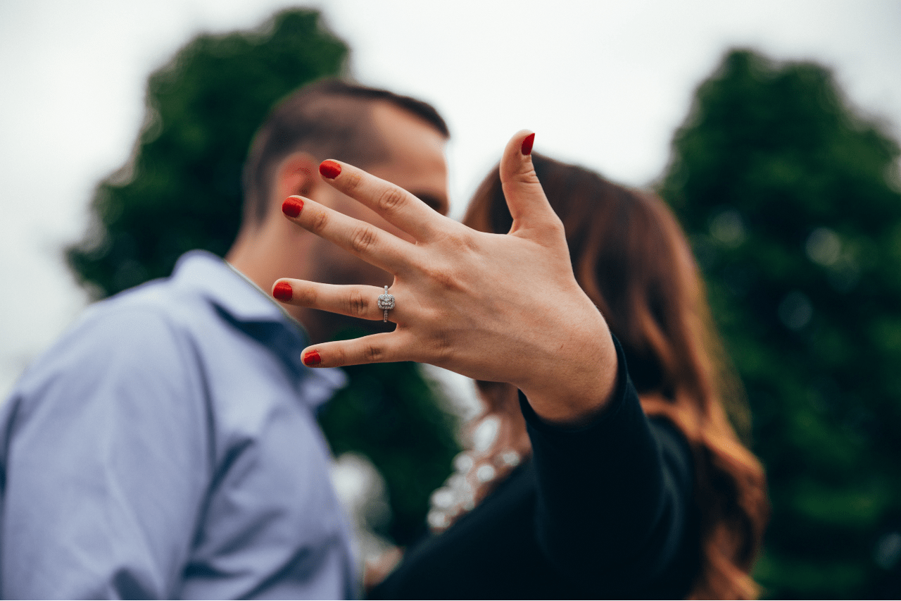 A recently engaged couple sharing a kiss, the bride-to-be’s hand in the foreground showing off her diamond engagement ring.