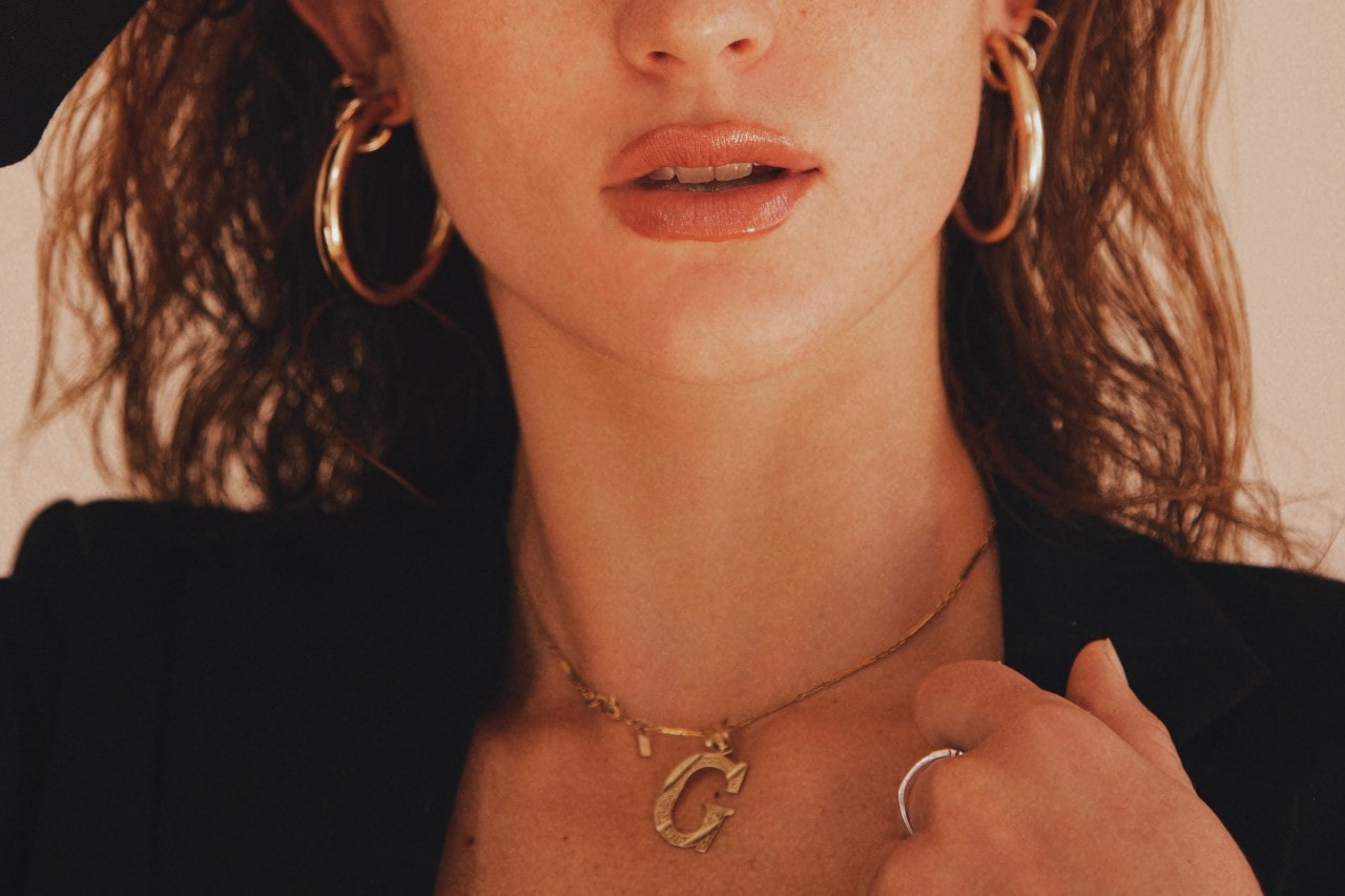 A woman wearing gold hoop earring and a gold “G” necklace.