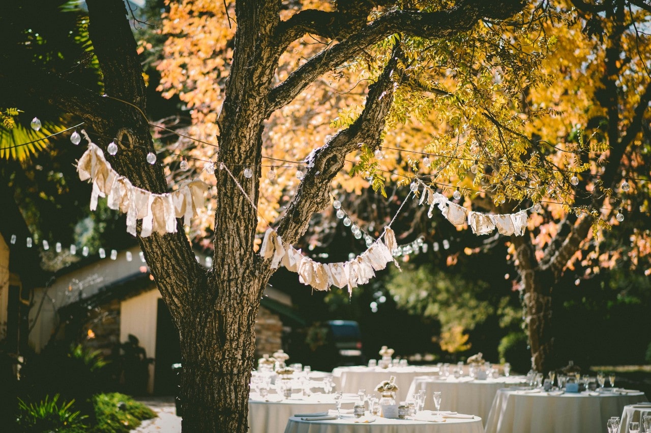 banners and string lights hung in a forest over white covered tables set for a wedding reception