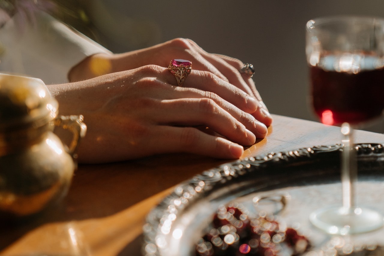 A woman’s hands wearing gemstone fashion rings, resting on a lavishly set table.