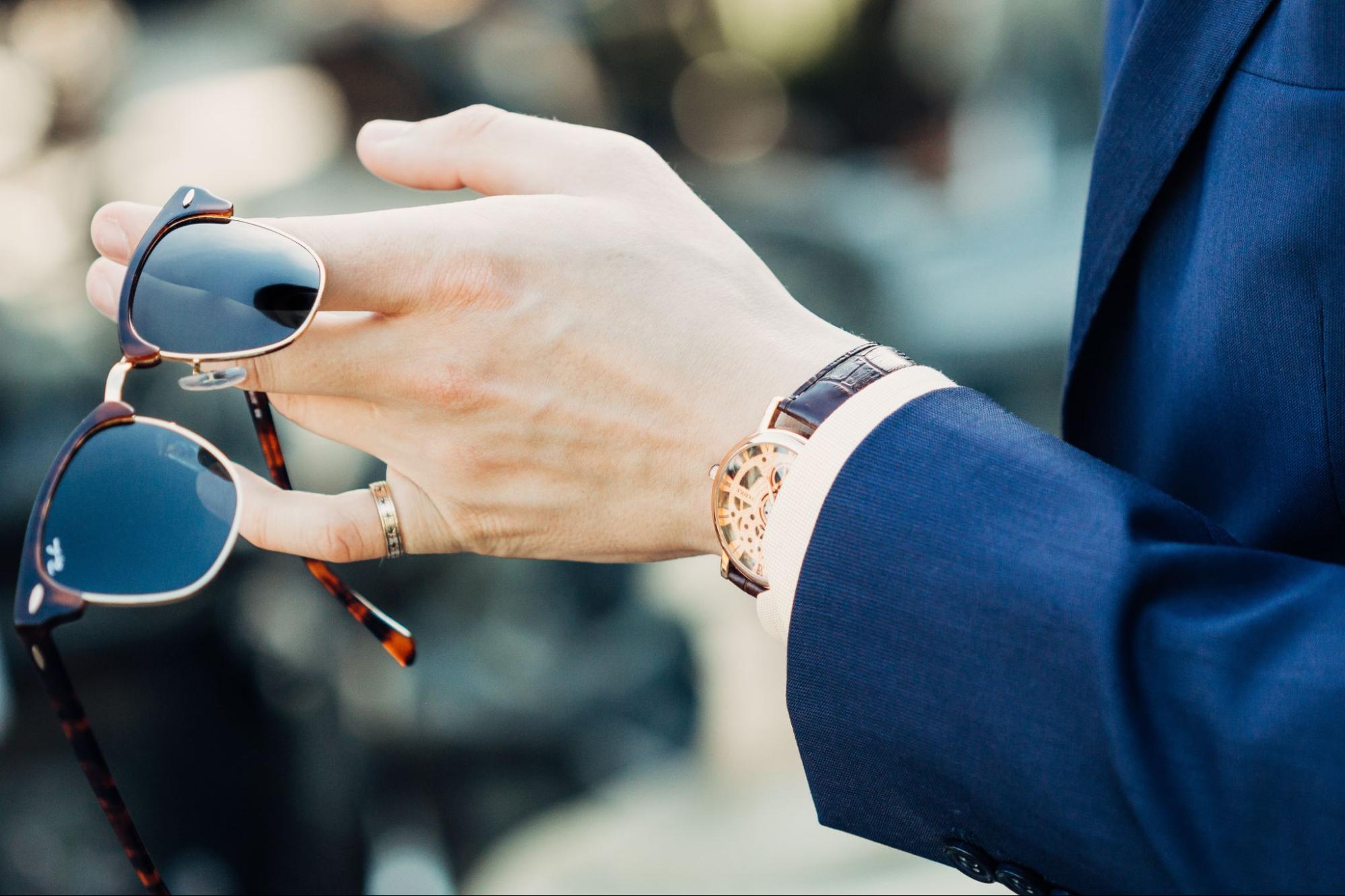 A well-dressed man in a blue suit wearing a gold pinky ring and dress watch.