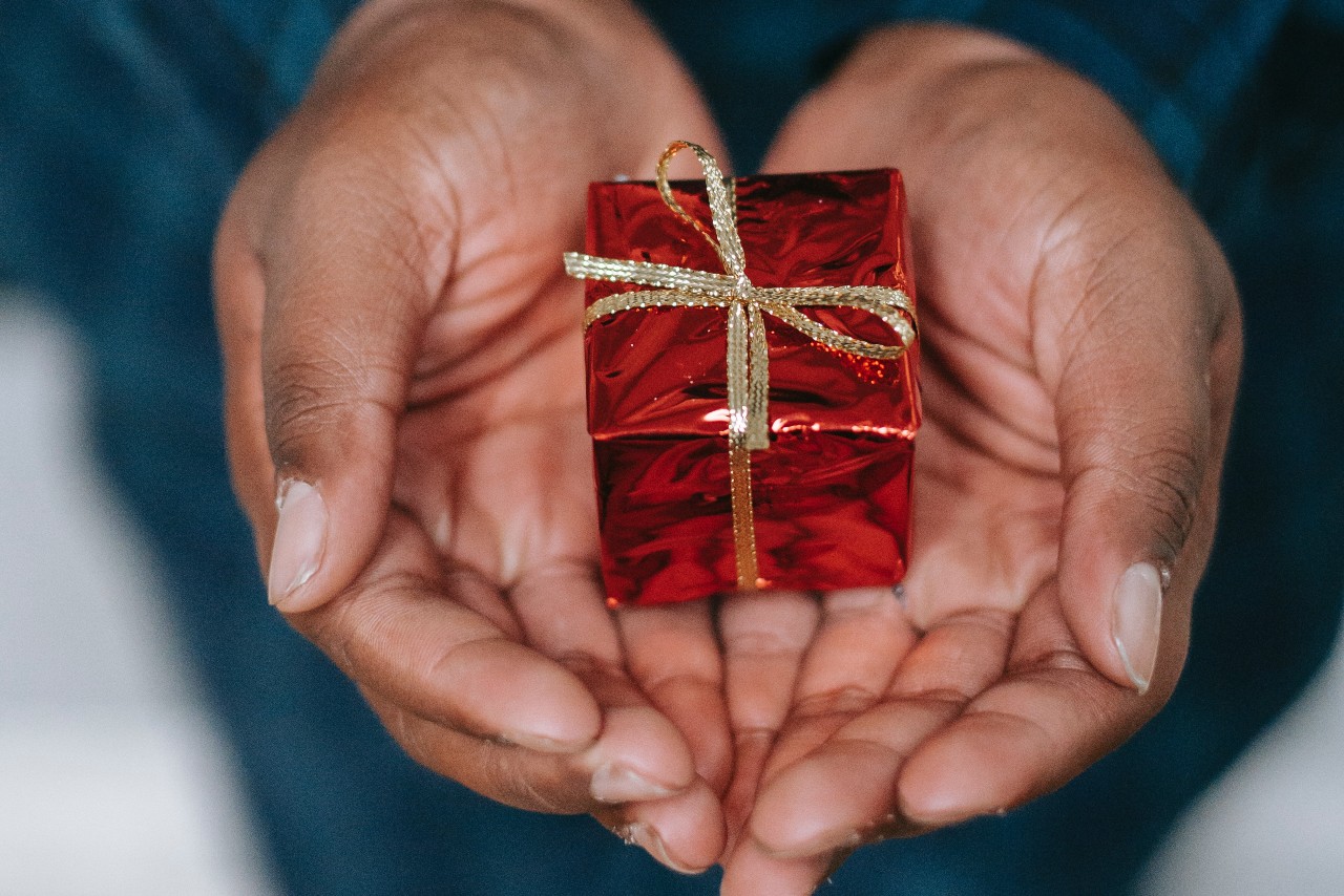 A person’s hands presenting a small gift to an out-of-view loved one.