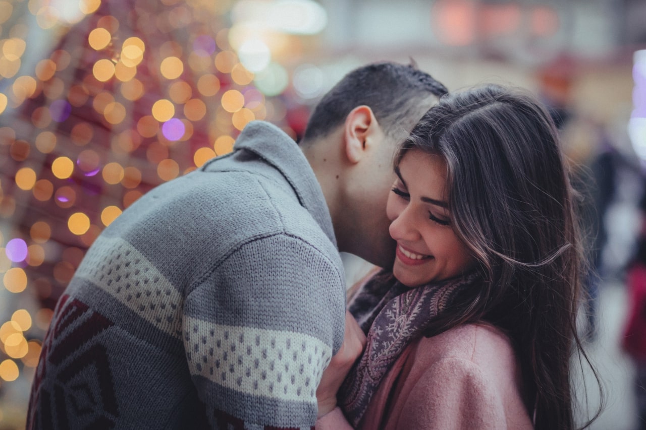 A young woman smiling as her significant other kisses her.