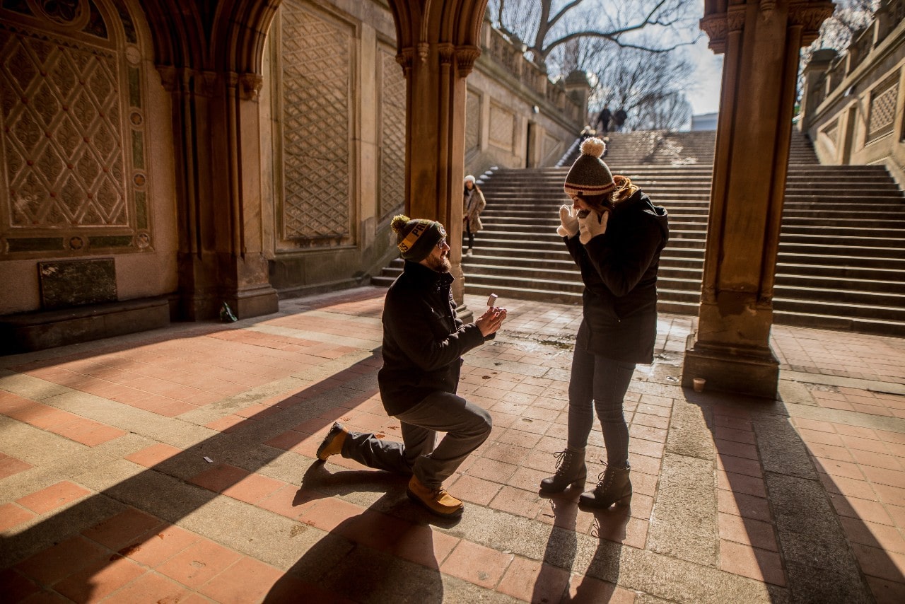 A young man proposing to his excited significant other during winter in a picturesque walkway.
