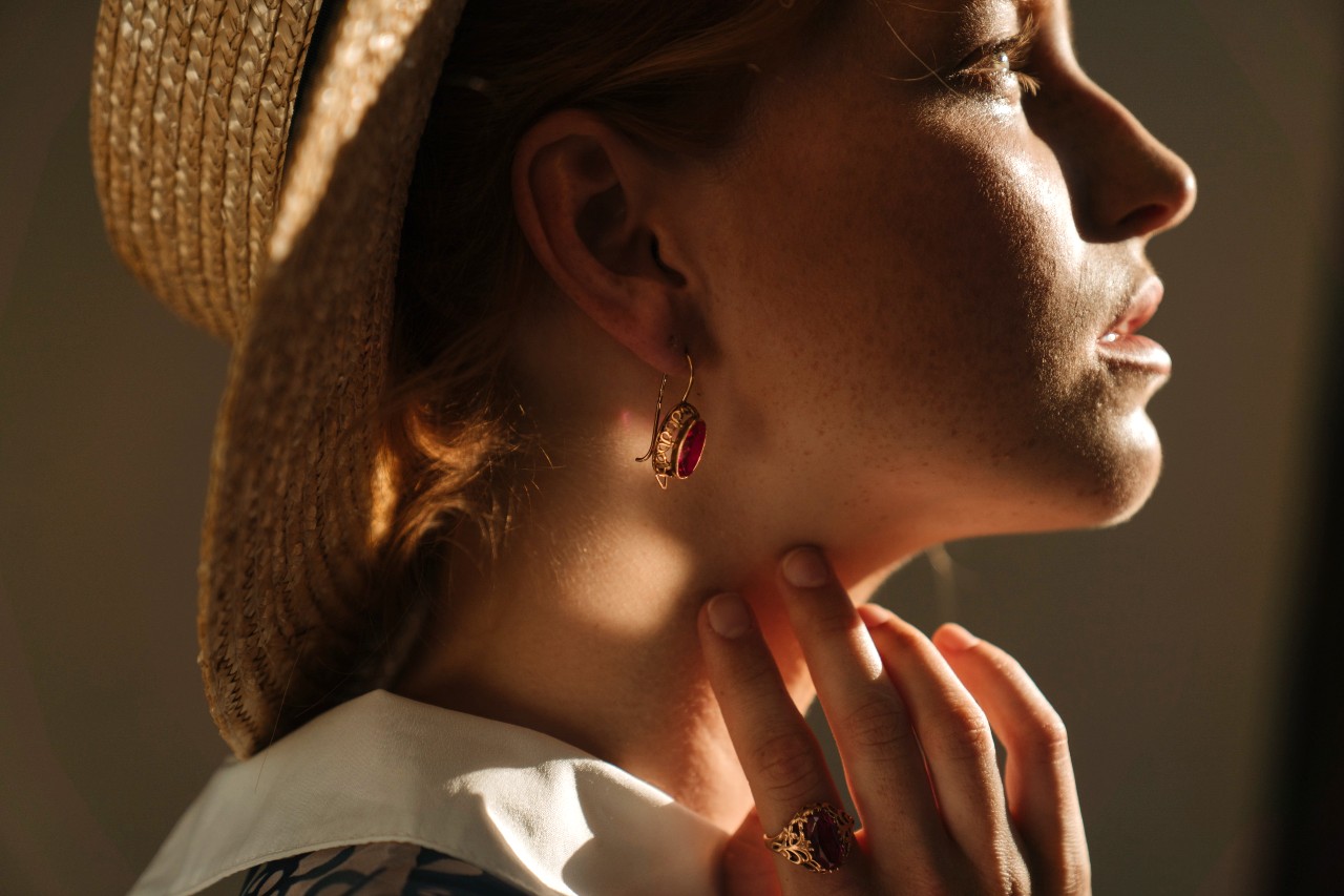 A woman in stylish gold jewelry under dappled sunlight.