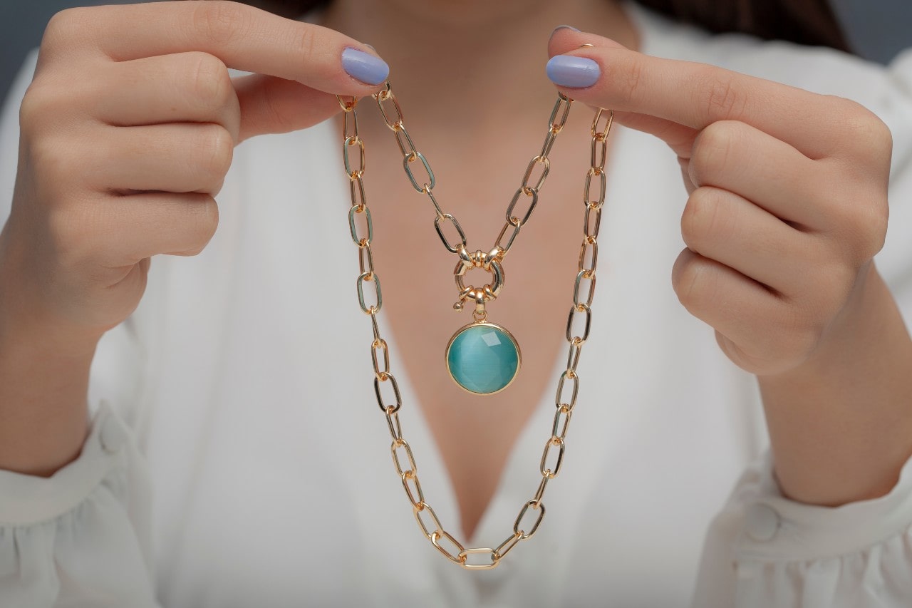 A close-up of a woman gently holding an elegant gold necklace.