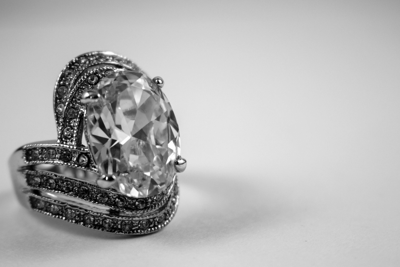 A black and white close-up of an opulent oval cut engagement ring.