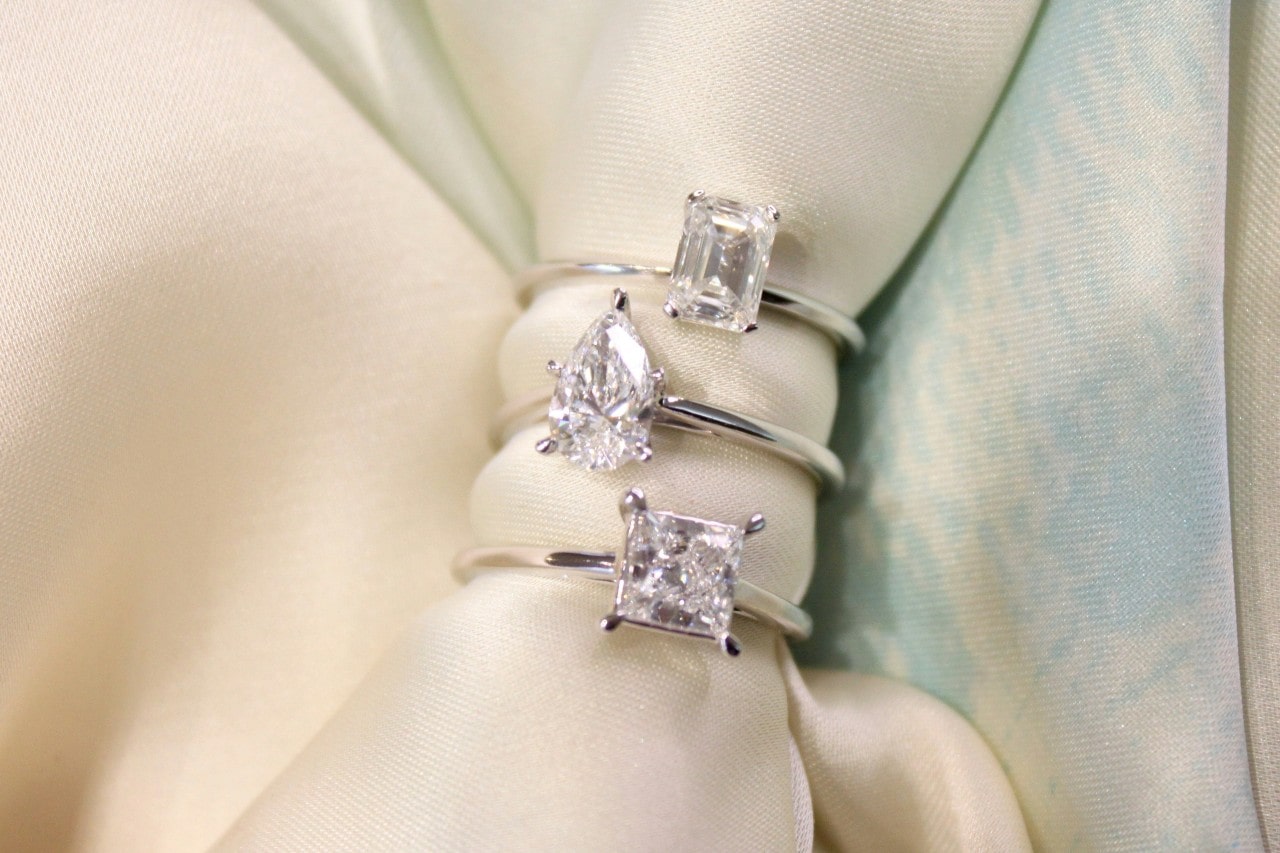 A close-up of three solitaire engagement rings with unique center stone shapes.