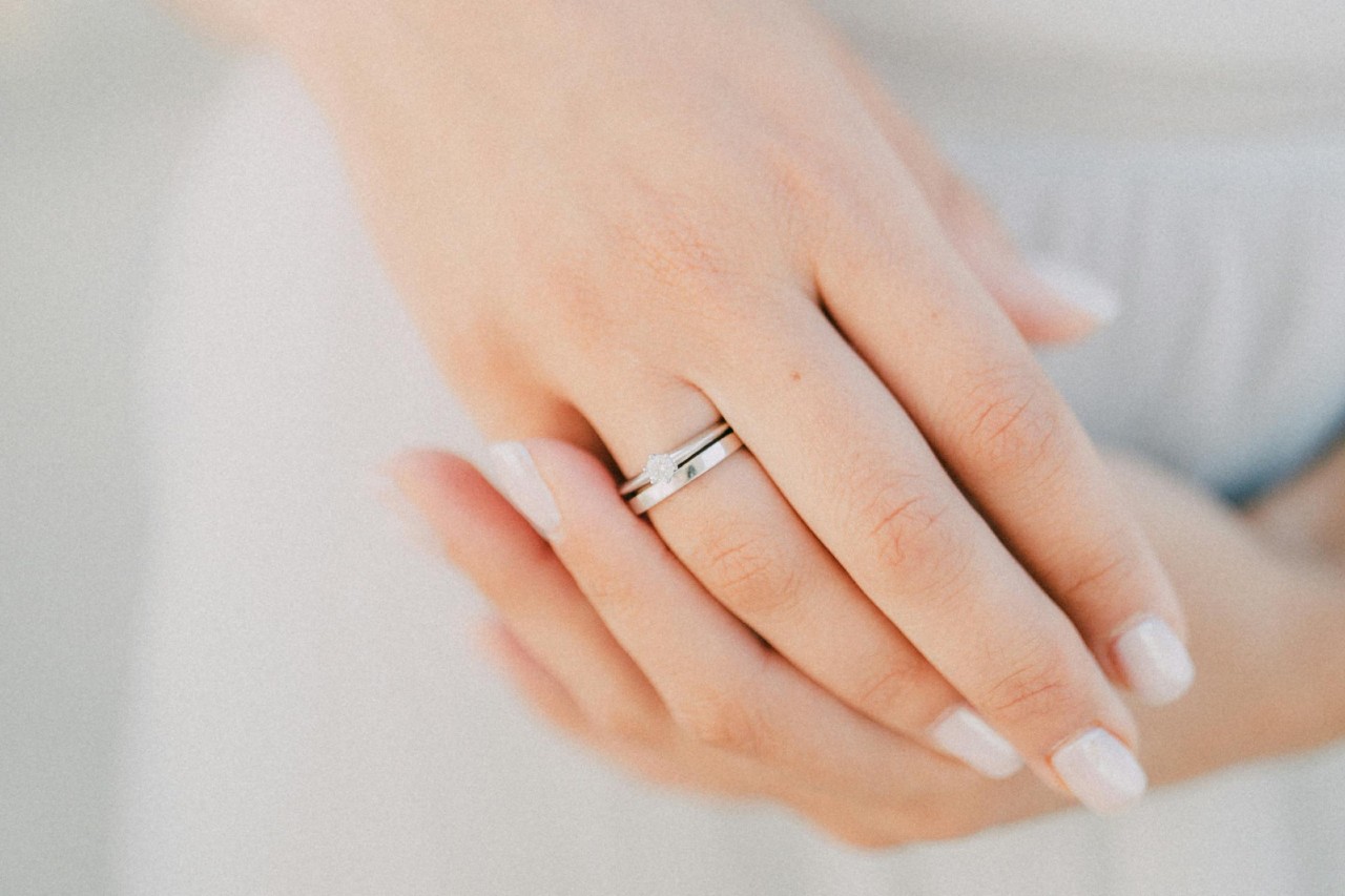 a closeup of a solitaire ring and a simple wedding band on a woman’s hand.