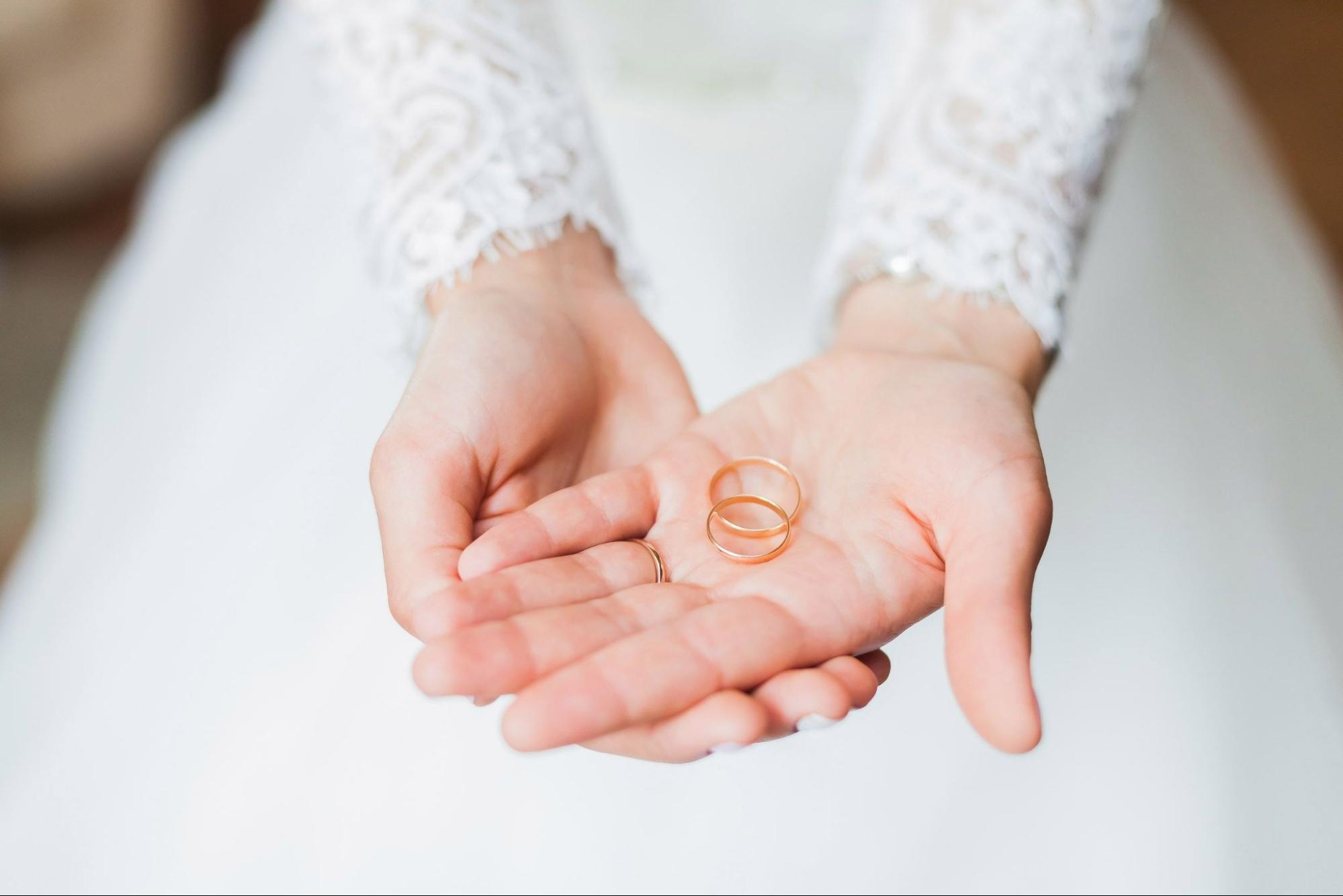 A bride holds two rose gold wedding rings in her palm.