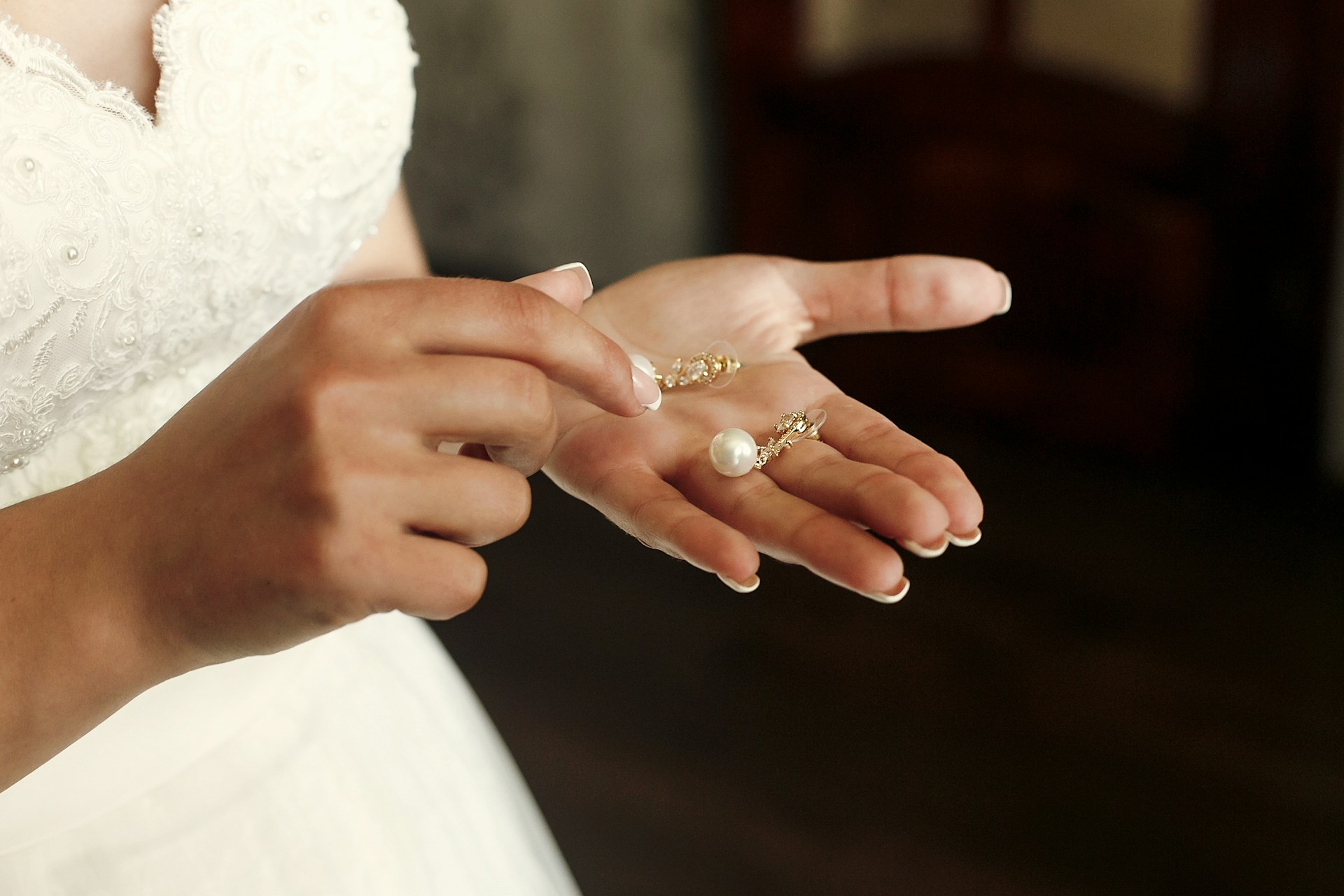 A bride in her wedding gown looking down at the pearl earrings in her hand.