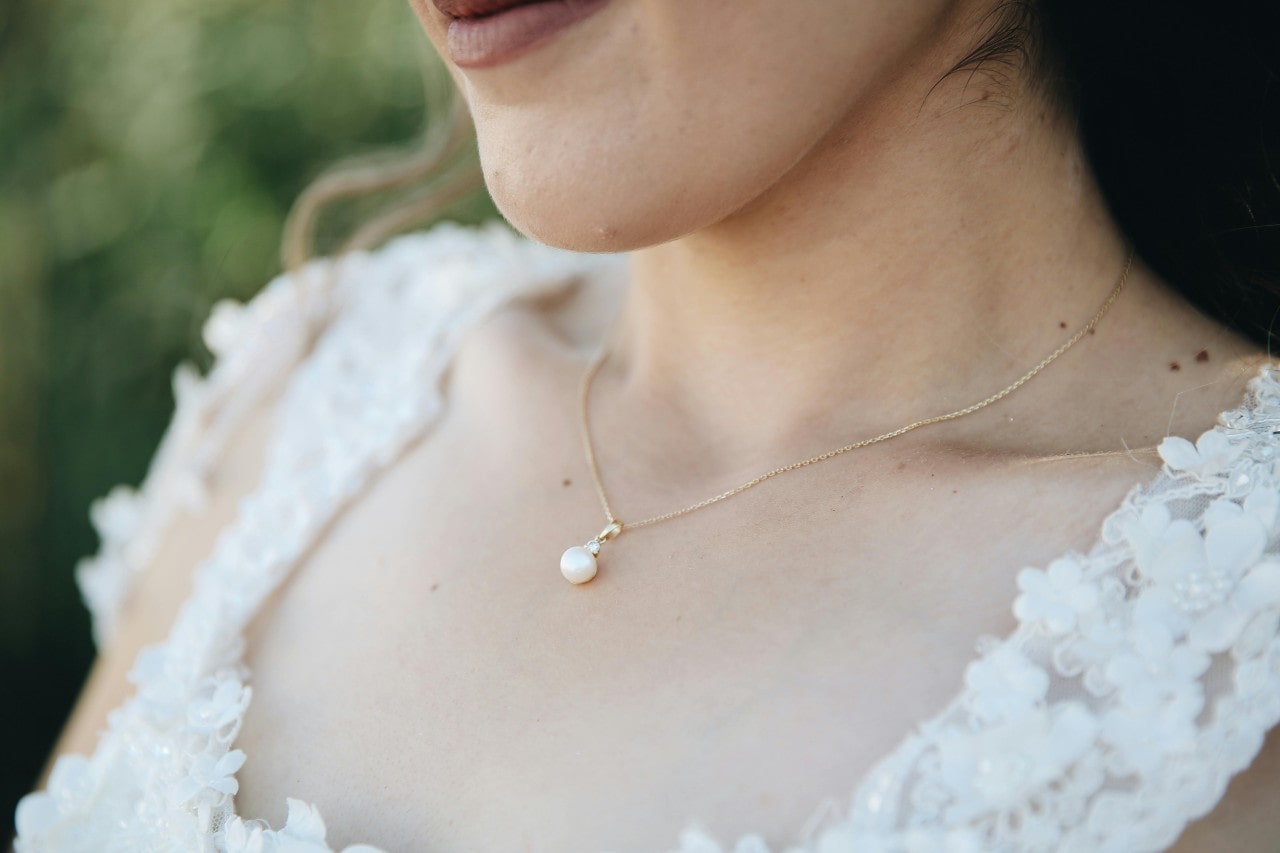 A bride’s neckline adorned with a simple pearl pendant necklace.