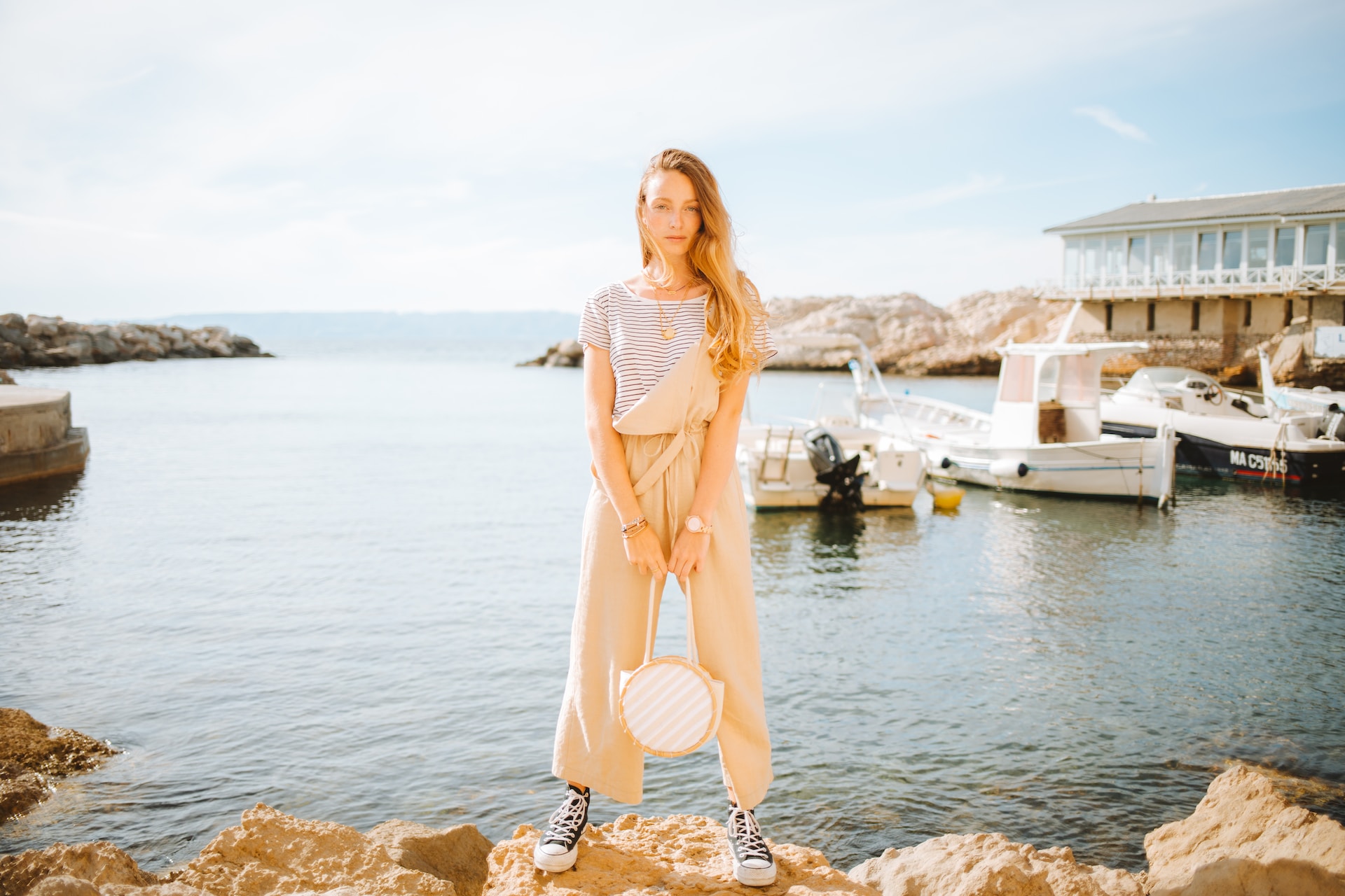 lady standing on some rocks by a body of water with some boats in the background