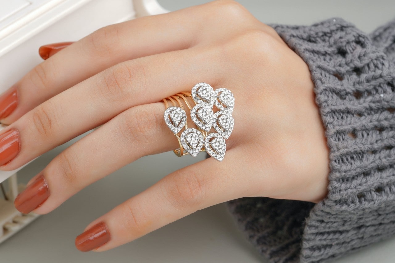 A close-up of a woman’s manicured hand wearing an ornate and opulent diamond fashion ring as an engagement ring.