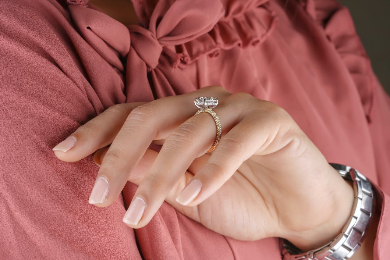 A close-up of a woman in a pink blouse wearing a vintage engagement ring